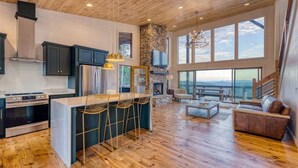A modern kitchen with a stone fireplace, wooden flooring, and a large dining area with bar stools. - Big Sky 2 - Hot tub & game room (Epworth)