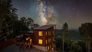 A wooden cabin with multiple windows and a staircase, surrounded by trees and a starry night sky. - Big Sky 2 - Hot tub & game room (Epworth)