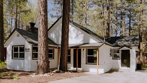 A small, single-story cabin with a white exterior, large windows, and a covered porch area. - NEWLY RENOVATED Pet Friendly Home (Big Bear Lake)