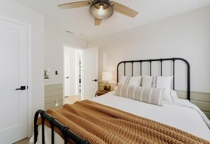A bedroom with a bed, a nightstand, a lamp, a ceiling fan, and a door.