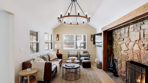 A cozy living room with a stone fireplace, a brown leather sofa, a round coffee table, and a chandelier. - NEWLY RENOVATED Pet Friendly Home (Big Bear Lake)