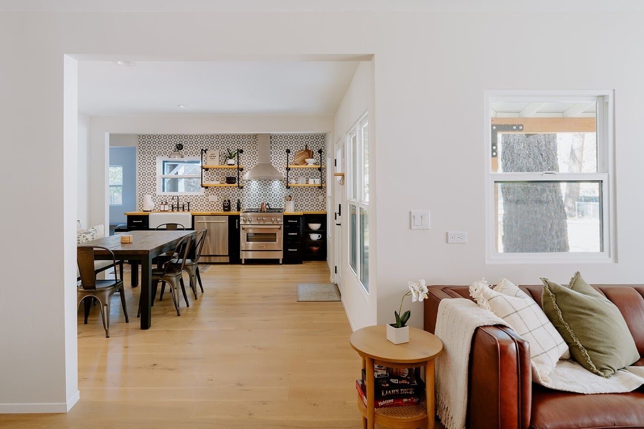 Eine moderne Küche mit Essbereich, Holzböden und einem gemütlichen Wohnbereich mit Ledersofa und kleinem Tisch.