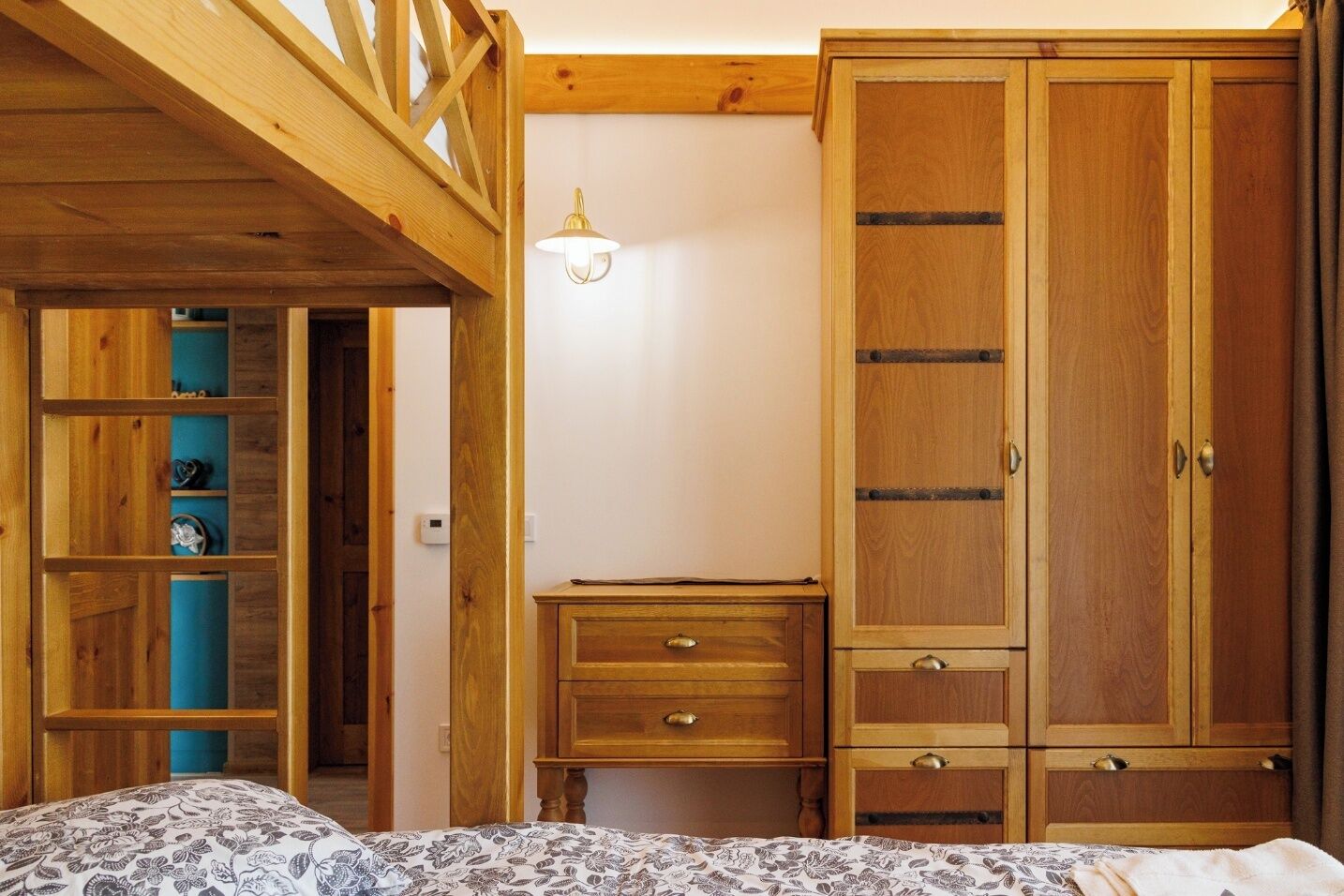 A bedroom with a bed, wooden wardrobe, a desk, and shelves.