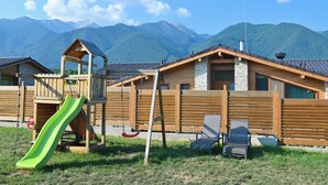 A wooden cabin with a green slide, a swing set, and a view of mountains. - Villa Raphael near Pirin Golf Resort (Razlog)