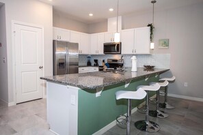 A modern kitchen with white cabinets, stainless steel appliances, a granite countertop, and a green accent wall. - 5158 Beautiful Villa 4bd/3.5bth Near Disney (Kissimmee)