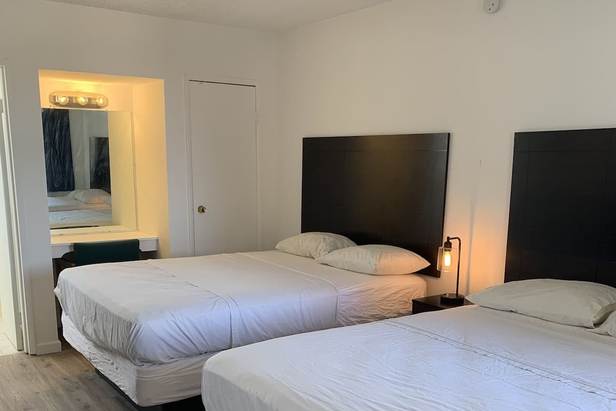A hotel room with two beds, a mirror, a vanity, and a door.