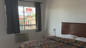 Une chambre avec un lit, une fenêtre avec des rideaux, un radiateur fixé au mur, et une vue sur l’enseigne d’un restaurant à l’extérieur.