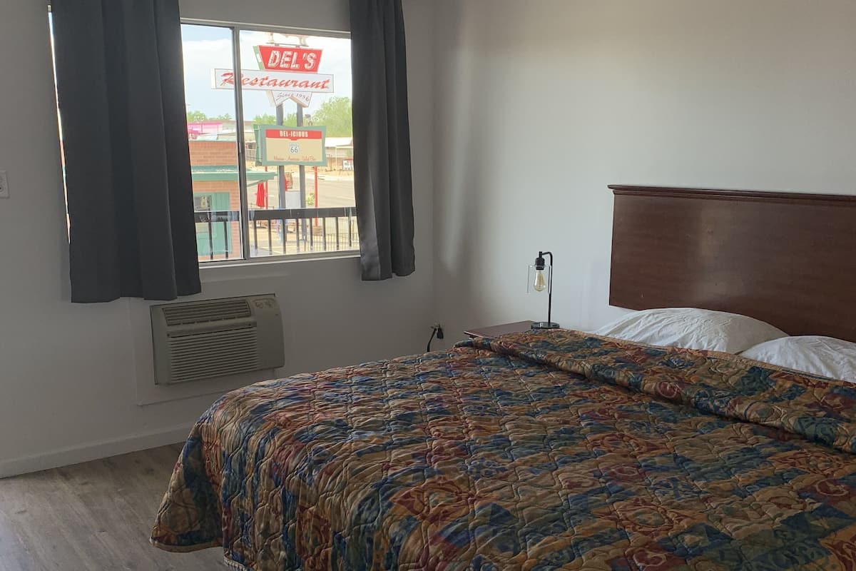 A bedroom with a bed, a window with curtains, a wall-mounted heater, and a view of a restaurant sign outside.