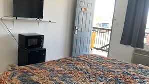 Une chambre avec un lit, un téléviseur fixé au mur, un four à micro-ondes posé sur une petite table et une porte portant le numéro 203.