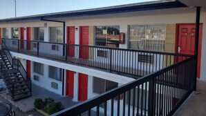 Un bâtiment avec plusieurs portes rouges, un balcon doté d’une rambarde noire et un ciel dégagé.