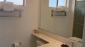 Une salle de bain avec des toilettes, un lavabo et un miroir. Il y a des serviettes sur une étagère au-dessus des toilettes et un rouleau de papier toilette accroché au mur.