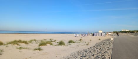 Uma praia com calçadão, guarda-sóis e céu claro.