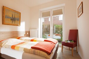 Ein Hotelzimmer mit zwei Betten, einem roten Sessel und einem großen Fenster mit Blick ins Grüne.