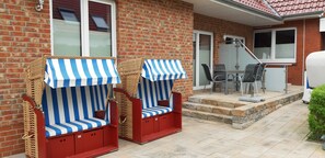Twee strandstoelen met strepen, een patio tafel en stoelen, voor een bakstenen muur met een betegeld dak.