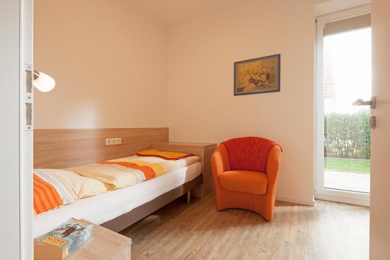 Un dormitorio con cama, una silla, una mesita y una ventana con vistas a zonas verdes.
