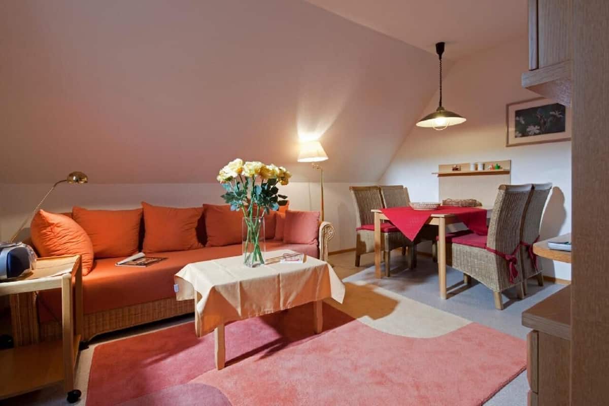 Un salón acogedor con un sofá, una mesa de comedor y un jarrón de flores.