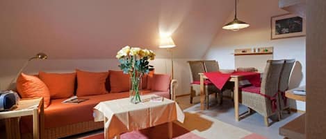 A cozy living room with a sofa, a dining table, and a vase of flowers.