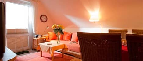 A cozy room with a sofa, a table with a vase of flowers, a lamp, and a clock on the wall.