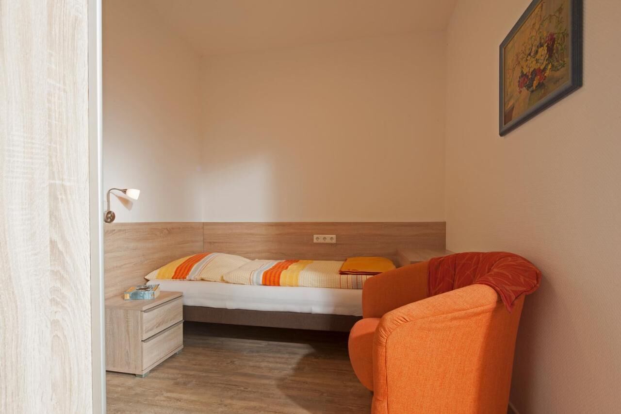 Een slaapkamer met een bed, nachtkastje en een oranje stoel.