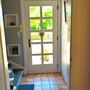 Een witte deur met zes ruiten, een decoratie in de vorm van een hart en een blauwe mat op de vloer.