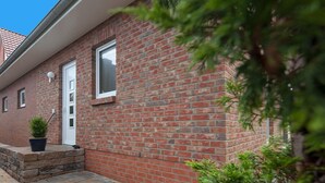 A brick building with a white door and windows, a small potted plant, and a stone ledge. - Ferienhaus Mien Huske (Norderney)