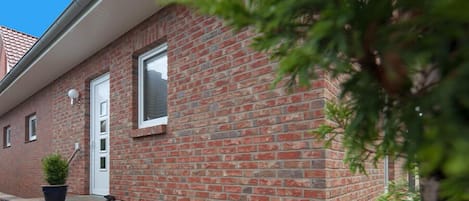 Un edificio de ladrillo con una puerta y ventanas blancas, una pequeña planta en maceta y un alféizar de piedra.