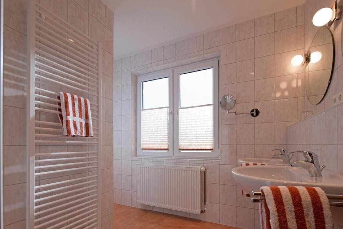 Een badkamer met twee wastafels, een spiegel en een raam met zonwering.