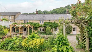 Ein Steinhhaus mit Garten, einer Holz-Pergola und einem Backsteinsschornstein.