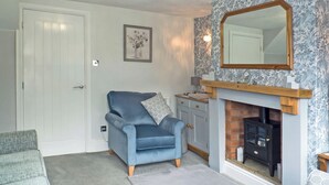 A living room with a blue armchair, a fireplace, a mirror, and a door.