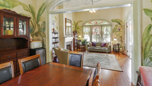 A dining area with a wooden table and chairs, a kitchen with a cabinet and microwave, and a living room with a sofa and a fireplace. - Auld Sweet Olive Bed & Breakfast (New Orleans)