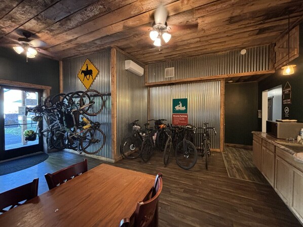 Un interior rústico con techos de madera, una zona de comedor y bicicletas estacionadas frente a una pared de metal corrugado.