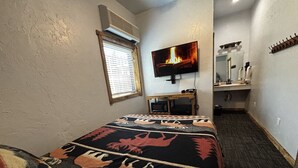 Une chambre d’hôtel avec un lit, une télévision, un petit bureau et un miroir.