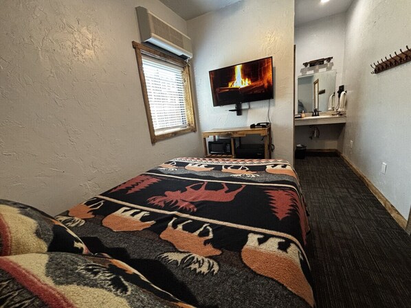 Una habitación de hotel con cama, televisión, escritorio pequeño y espejo.