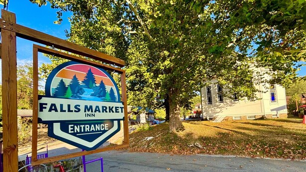 Une enseigne indiquant l’entrée du Falls Market Inn, avec un motif représentant une montagne et un arbre.