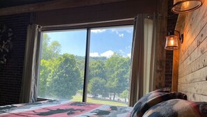 A bedroom with a large window, a bed with a patterned blanket, and a wall-mounted light fixture. - Falls Market Inn Riverview, Bike Trail, Fallingwater Hotel, 1 KIng Bed 1 Futon (Ohiopyle)