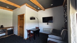 A compact room with a wooden door, a television mounted on the wall, a small table with chairs, and a sofa. - Falls Market Inn Riverview, Bike Trail, Fallingwater Hotel, 1 KIng Bed 1 Futon (Ohiopyle)