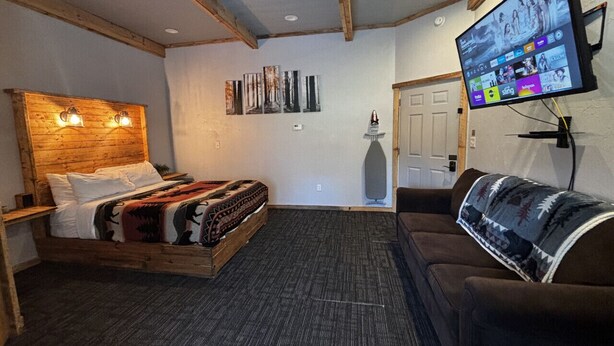 A room with a bed, a couch, a TV mounted on the wall, and a ceiling fan.