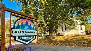 A sign for Falls Market Inn entrance with a mountain and tree design.