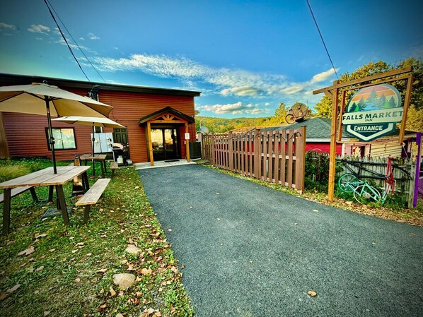 A building with a wooden exterior, a covered patio area with tables and benches, and a sign indicating the entrance to Falls Market Inn. - Ohiopyle Trailside Hotel Room 1 Queen Beds Sleeps 2 /Minutes to Fallingwater (Ohiopyle)