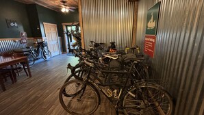 A room with wooden flooring, a dining area with a table and chairs, and bicycles parked against a corrugated metal wall. - Ohiopyle Trailside Hotel Room 1 Queen Beds Sleeps 2 /Minutes to Fallingwater (Ohiopyle)