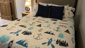 A bed with a quilt featuring nautical designs, a wooden headboard, and a nightstand with a lamp. - Ohiopyle Trailside Hotel Room 1 Queen Beds Sleeps 2 /Minutes to Fallingwater (Ohiopyle)