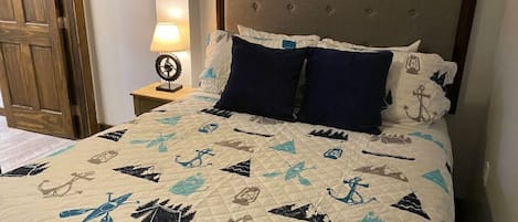 Ein Bett mit einer Decke mit Meeresmotiven, einem hölzernen Kopfteil und einem Nachttisch mit Lampe.