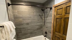 Une salle de bain avec une baignoire, un plancher en bois et une porte en bois.