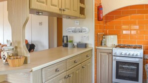 A kitchen with wooden cabinets, a white countertop, a stove, and a fire extinguisher. - Y Nyth Yn Bwthyn Coed Gellyg (Dinas Dinlle, near Caernarfon)