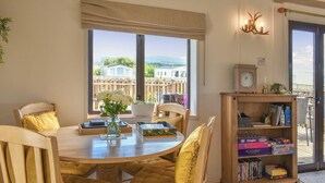 A dining area with a round table, wooden chairs, a bookshelf, and a view of the outside. - Y Nyth Yn Bwthyn Coed Gellyg (Dinas Dinlle, near Caernarfon)