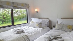 A bedroom with two beds, a window with a view of greenery, and a wall-mounted light. - Y Nyth Yn Bwthyn Coed Gellyg (Dinas Dinlle, near Caernarfon)