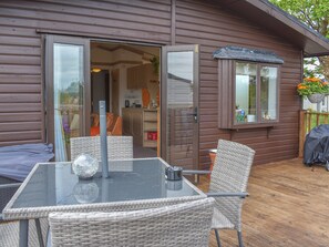 Ein Tisch mit Glasplatte und Korbstühle auf einer Holzterrasse einer Hütte.
