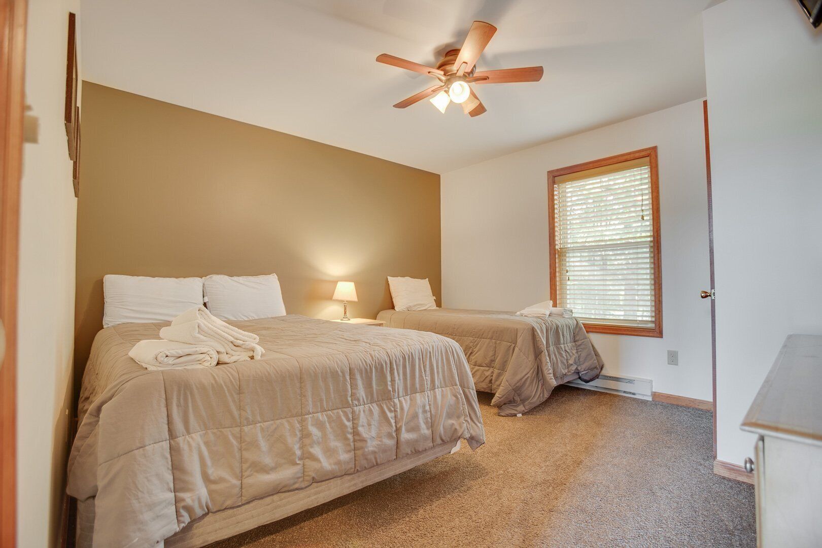 Une chambre avec deux lits, un ventilateur de plafond, une fenêtre avec des stores et une porte.