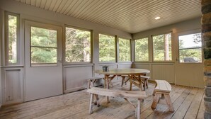 Un patio cubierto con mesa y bancos de madera, ventanas amplias y pared de piedra.
