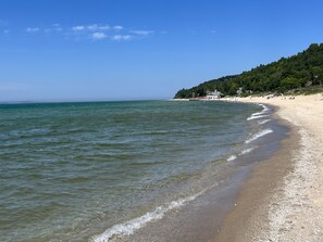A beach with clear water, a sandy shore, and a forested hill in the background.